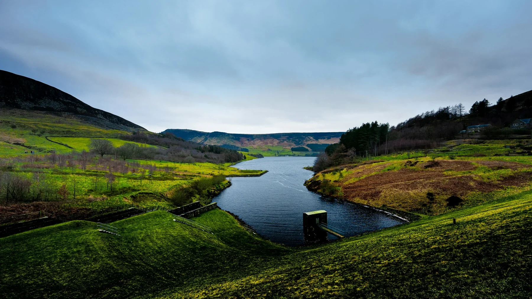 A freshwater reservoir curves between green hills beneath an overcast sky.